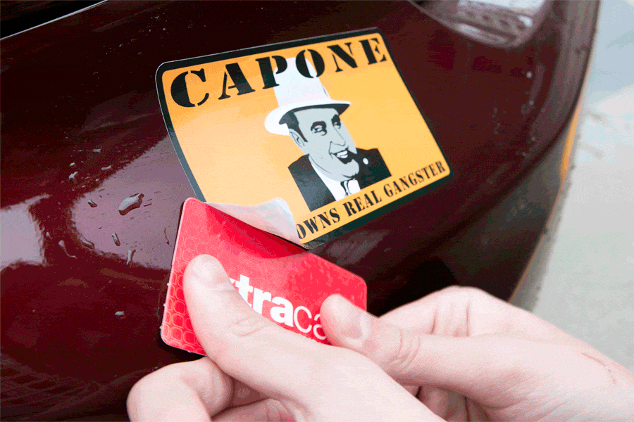 Using a plastic card to remove a sticker from a car